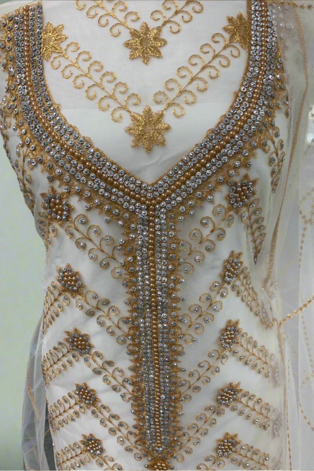 Close-up of a white garment with gold and silver embroidery on a mannequin.