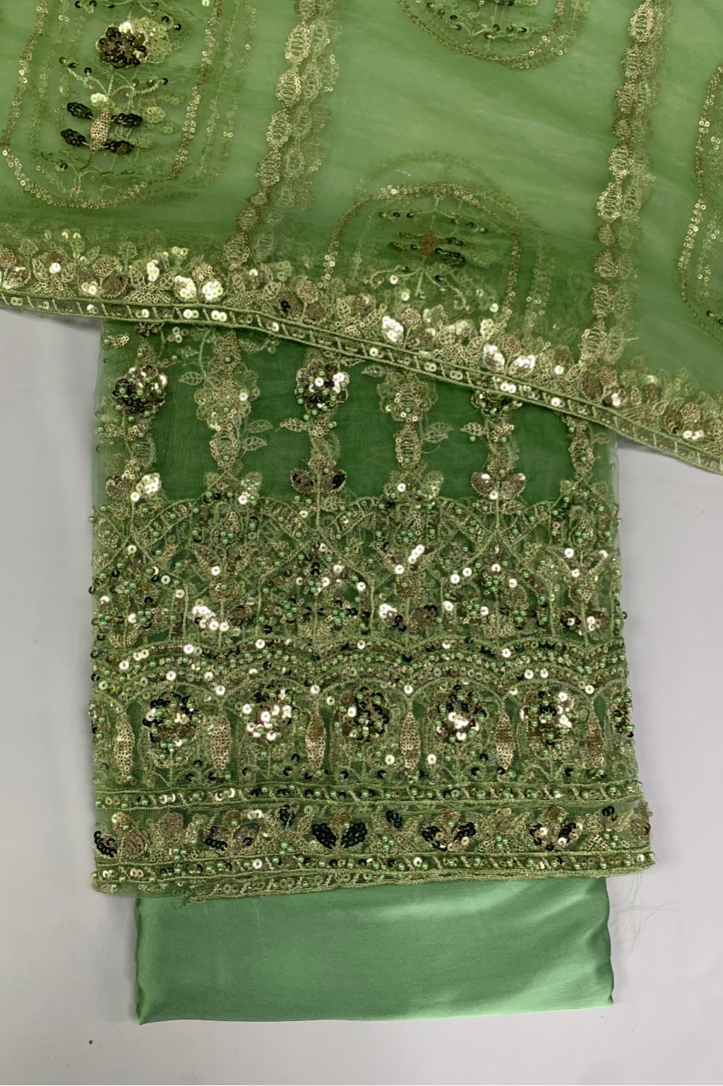 Green fabric with intricate gold and silver embroidery on a gray background
