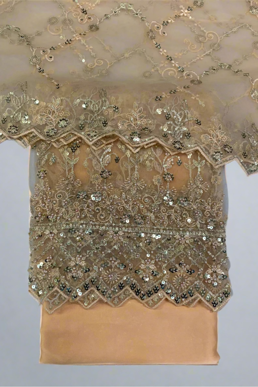 Peach fabric with intricate gold embroidery and sequin detailing on a white background