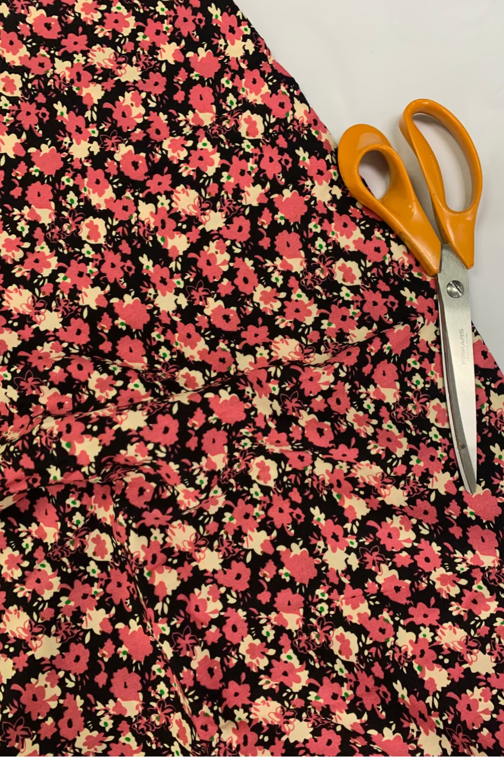 Floral fabric with pink and yellow flowers on a black background, accompanied by orange-handled scissors.