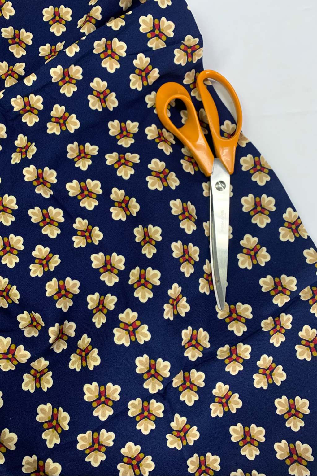 Floral-patterned fabric with a pair of orange-handled scissors on a white background