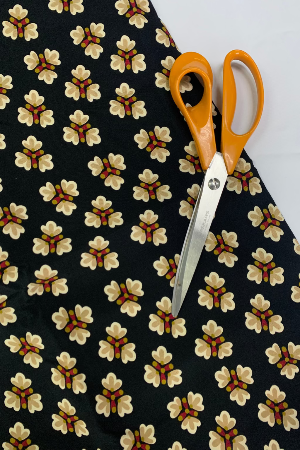Floral-patterned fabric with a pair of orange-handled scissors on a white background