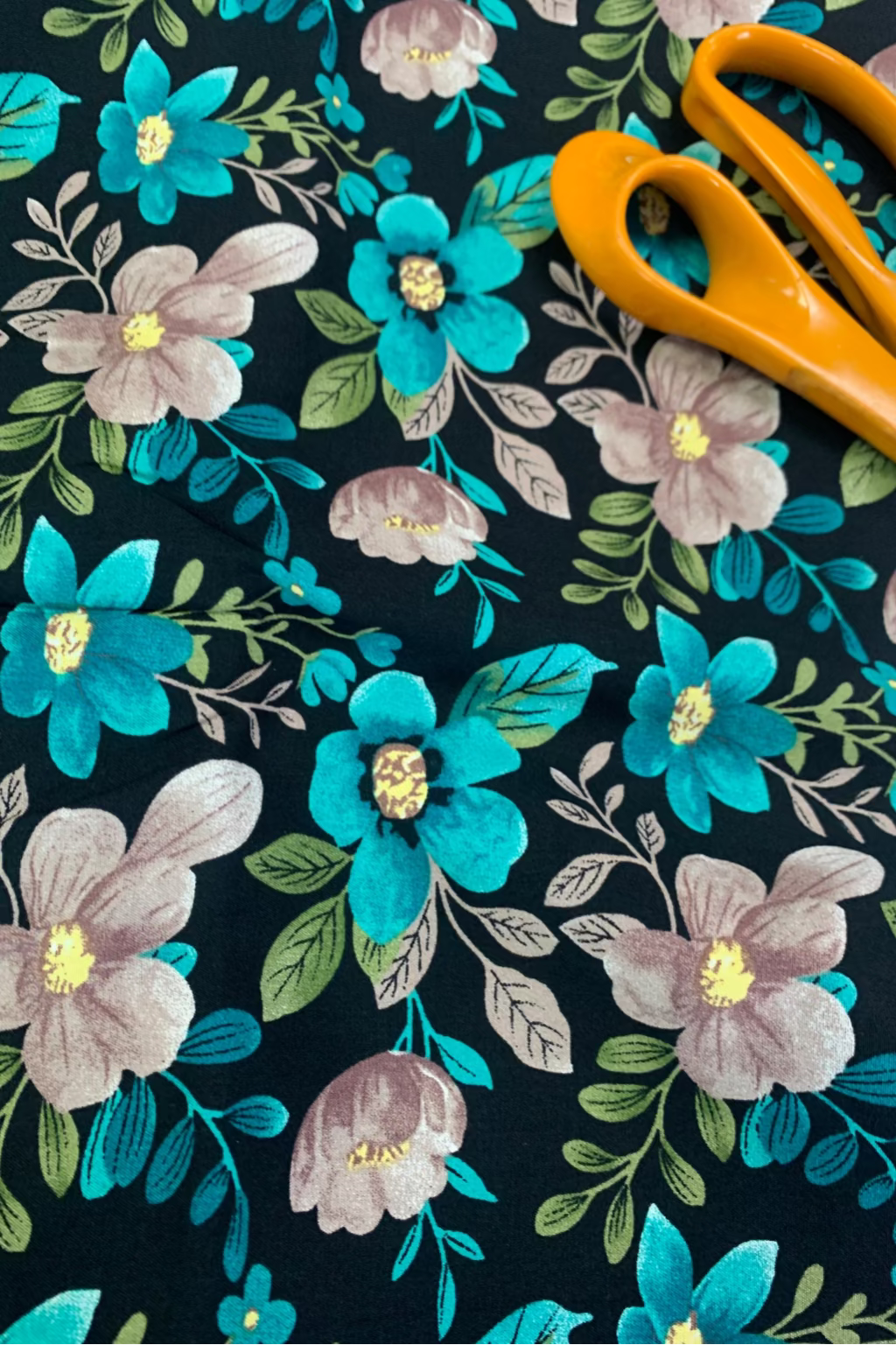 Floral fabric with blue and beige flowers on a dark background, accompanied by orange scissors.