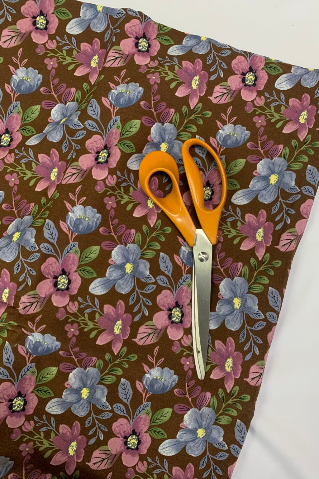 Floral-patterned fabric with orange-handled scissors on a white background