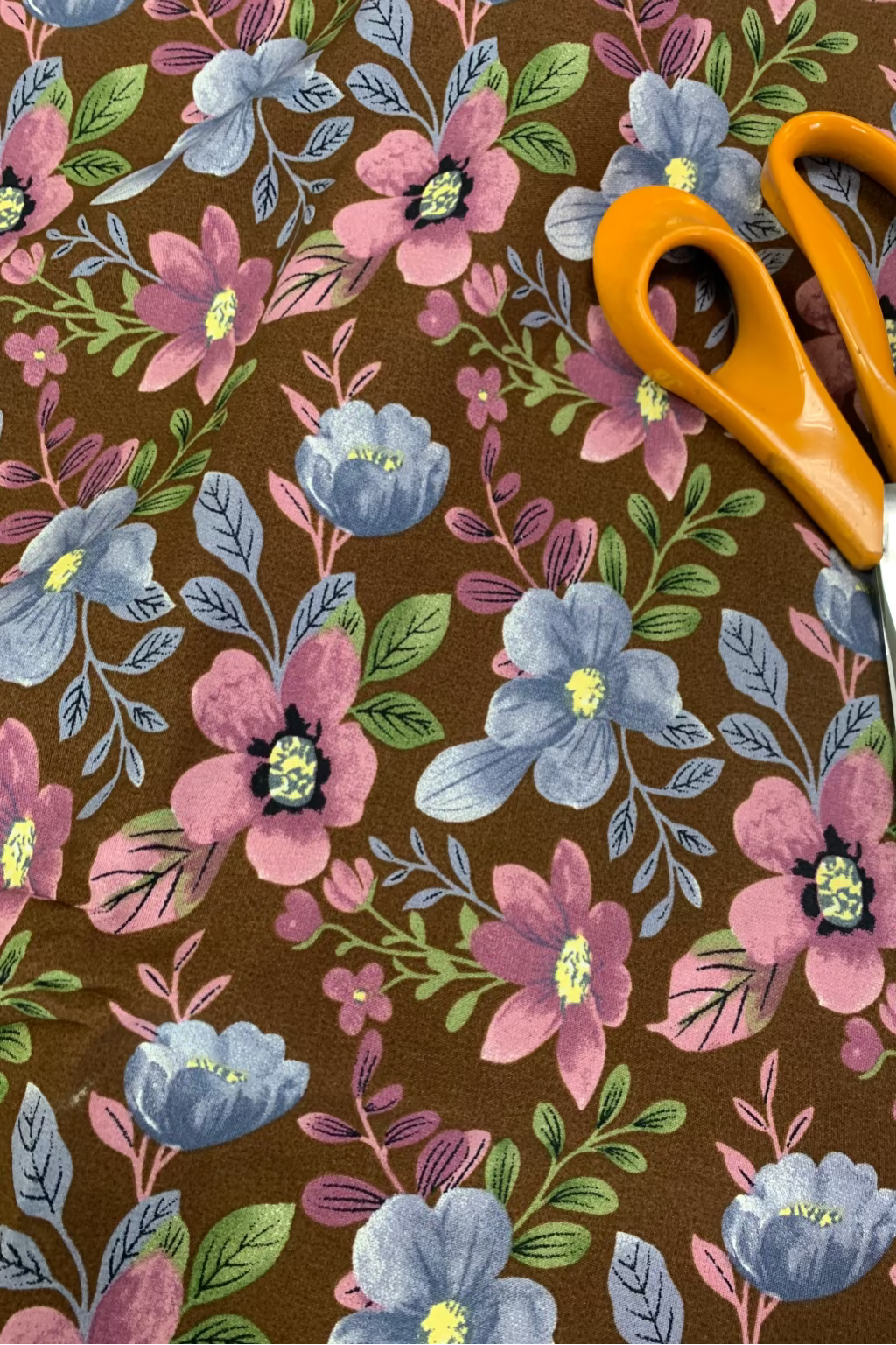 Floral fabric with pink and blue flowers on a brown background, accompanied by orange-handled scissors.