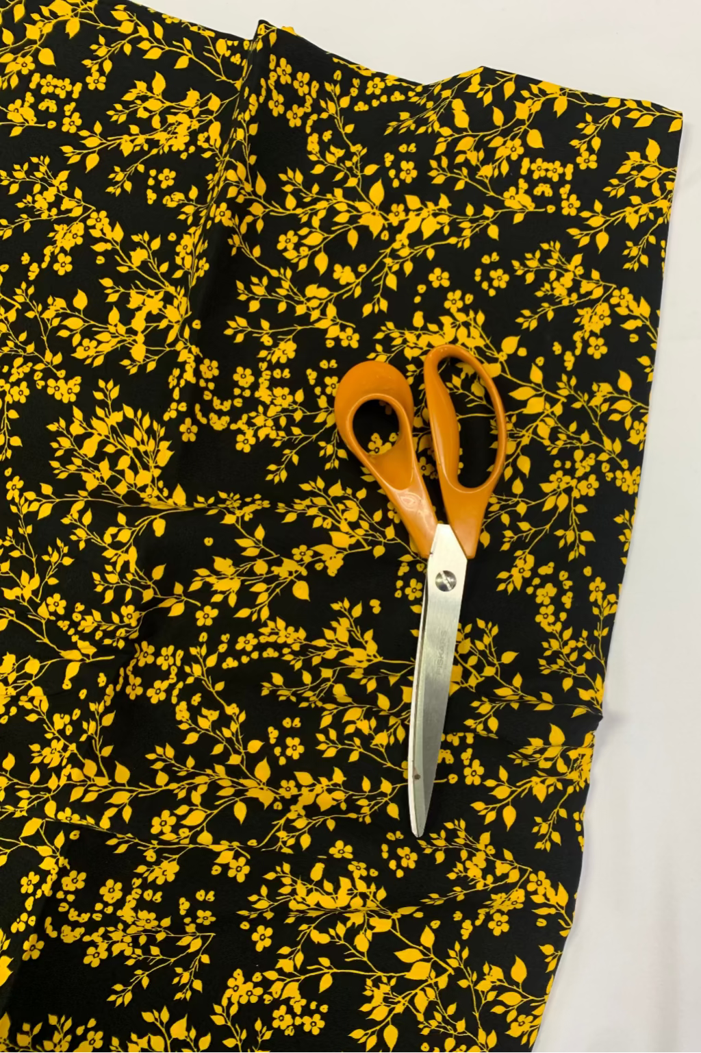 Black fabric with yellow floral pattern and a pair of scissors on a white background