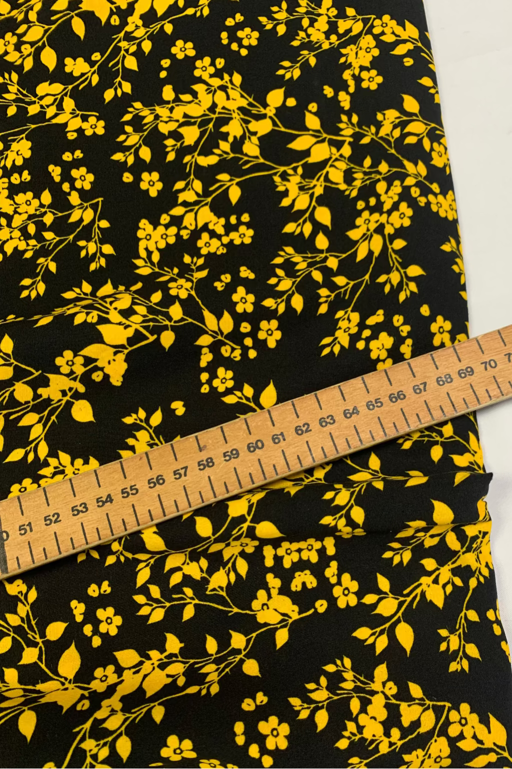 Black fabric with yellow floral pattern and a wooden ruler for scale.