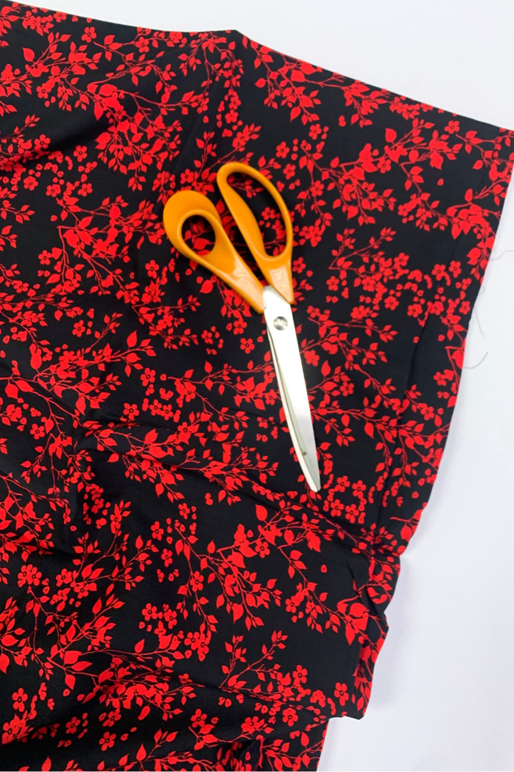 Pair of orange-handled scissors on a black fabric with red floral pattern