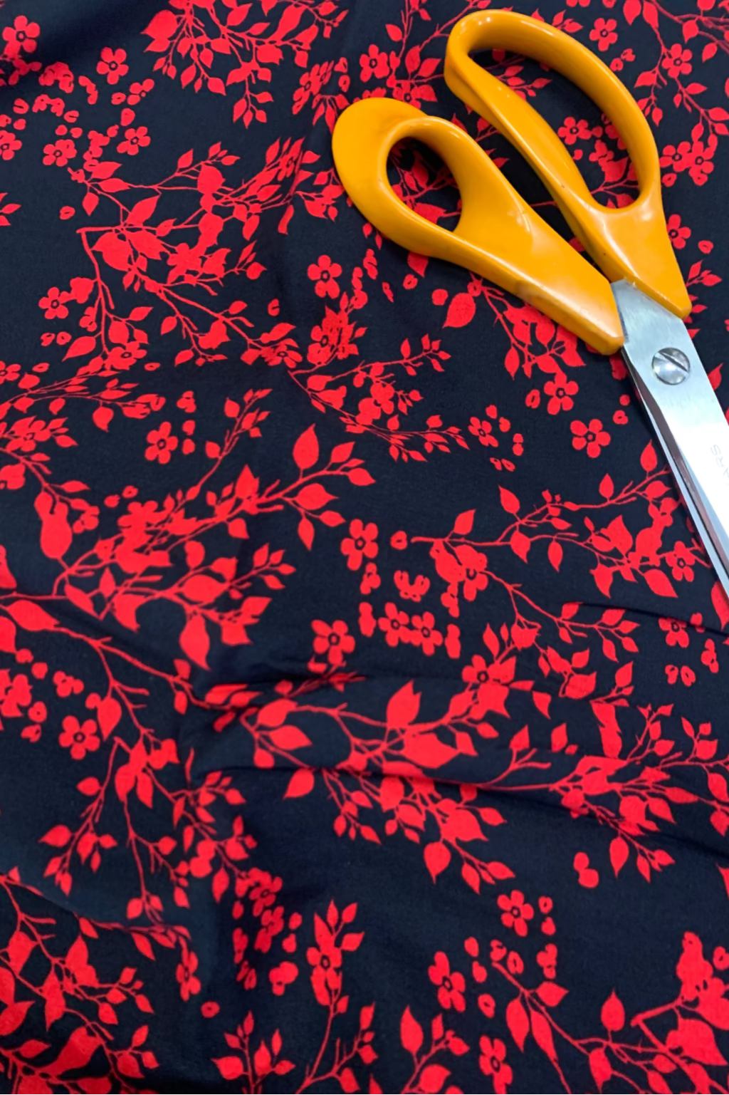 Scissors with yellow handles on a dark fabric with red floral pattern