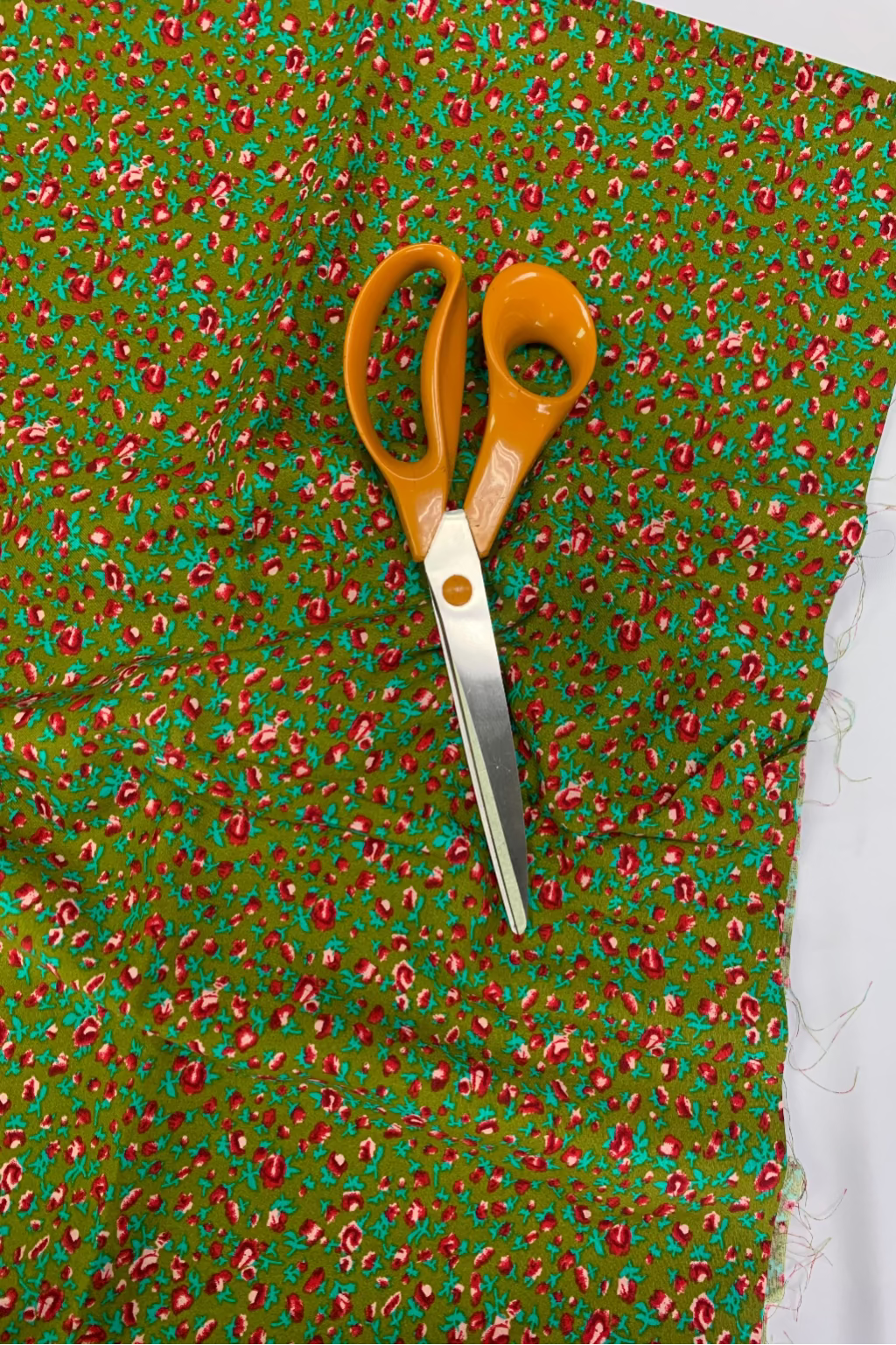 Pair of scissors on a piece of green fabric with a floral print.