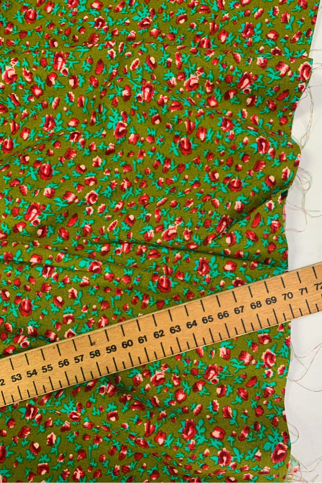 Green fabric with red floral pattern and a wooden ruler for scale.