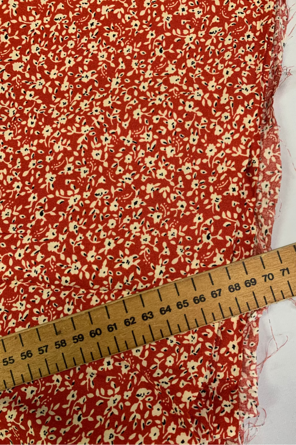 Red floral fabric with a wooden ruler for scale on a white background