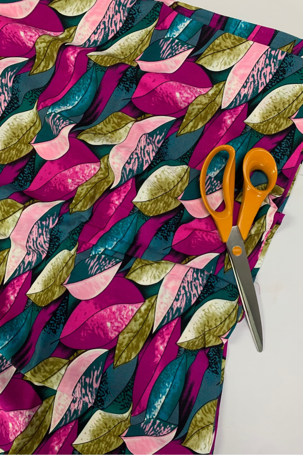 Colorful leaf-patterned fabric with a pair of orange-handled scissors on a white background