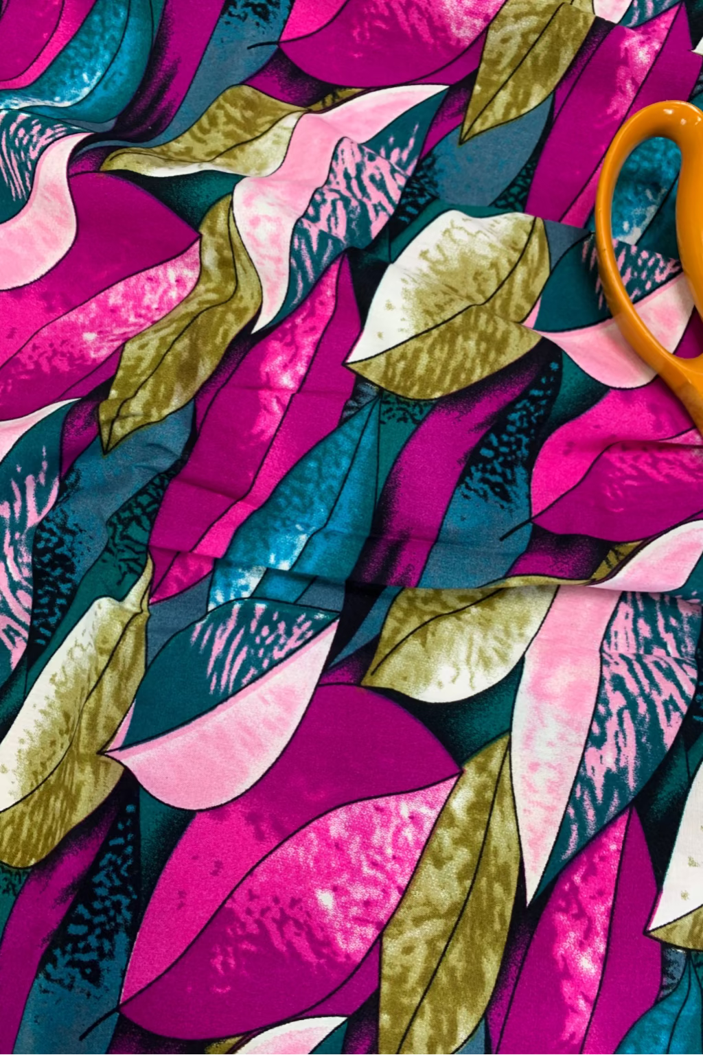 Colorful fabric with leaf pattern and orange scissors on top