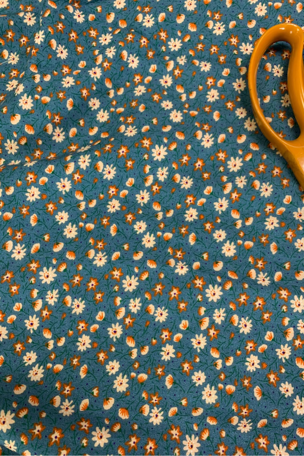Floral fabric with small white and orange flowers on a blue background, with a pair of yellow scissors.