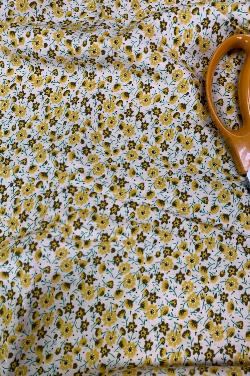Floral fabric with yellow flowers and green leaves, accompanied by a pair of scissors.