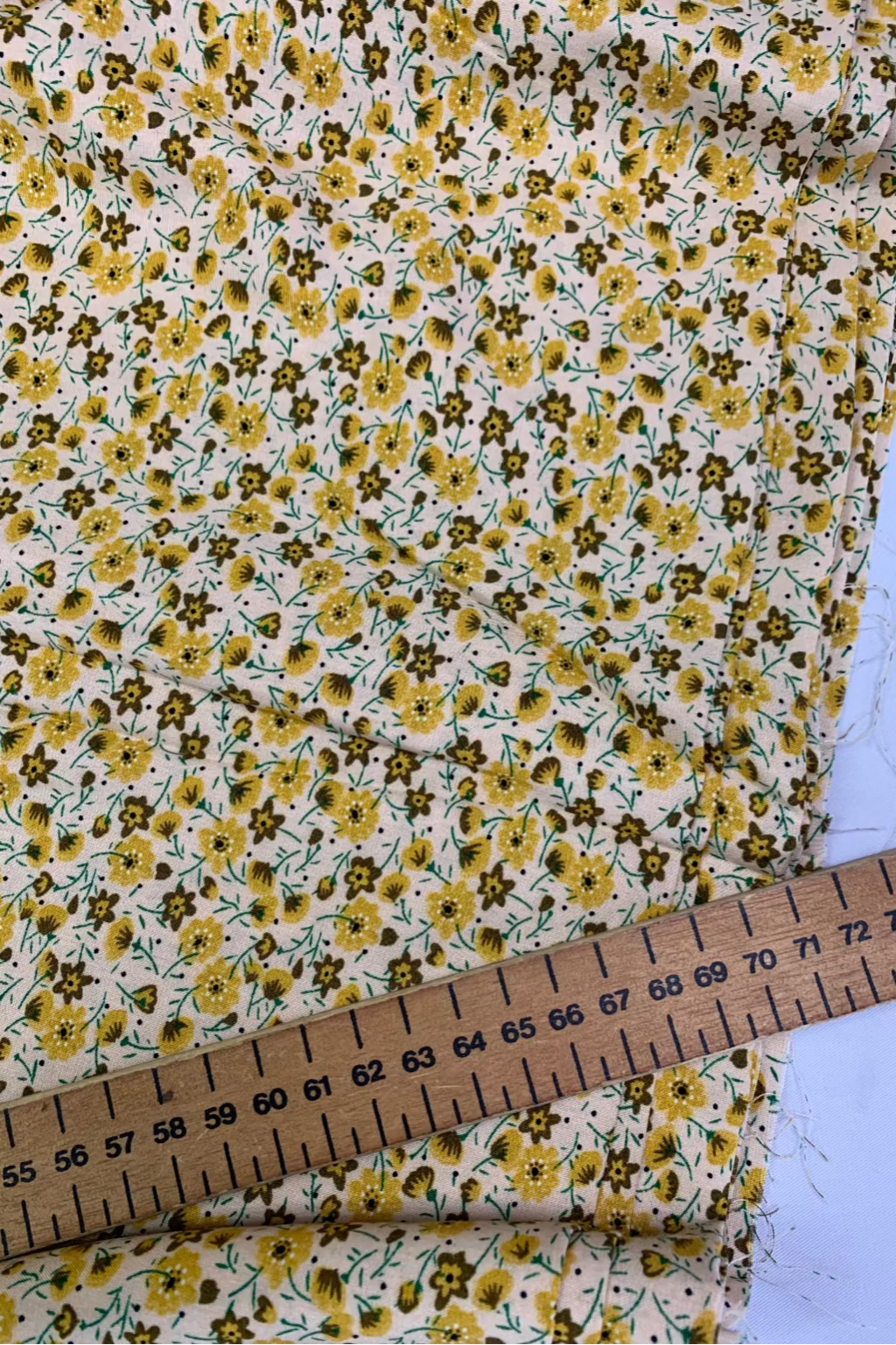 Floral fabric with yellow flowers on a white background, measured by a wooden ruler.