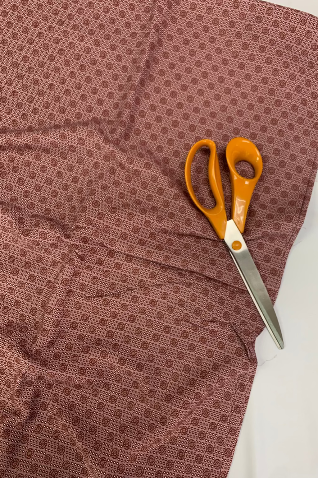 Pair of orange-handled scissors on a soft pink patterned fabric