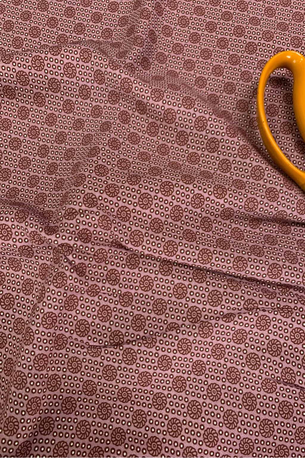 Soft pink fabric with a subtle pattern on a flat surface with a pair of scissors.