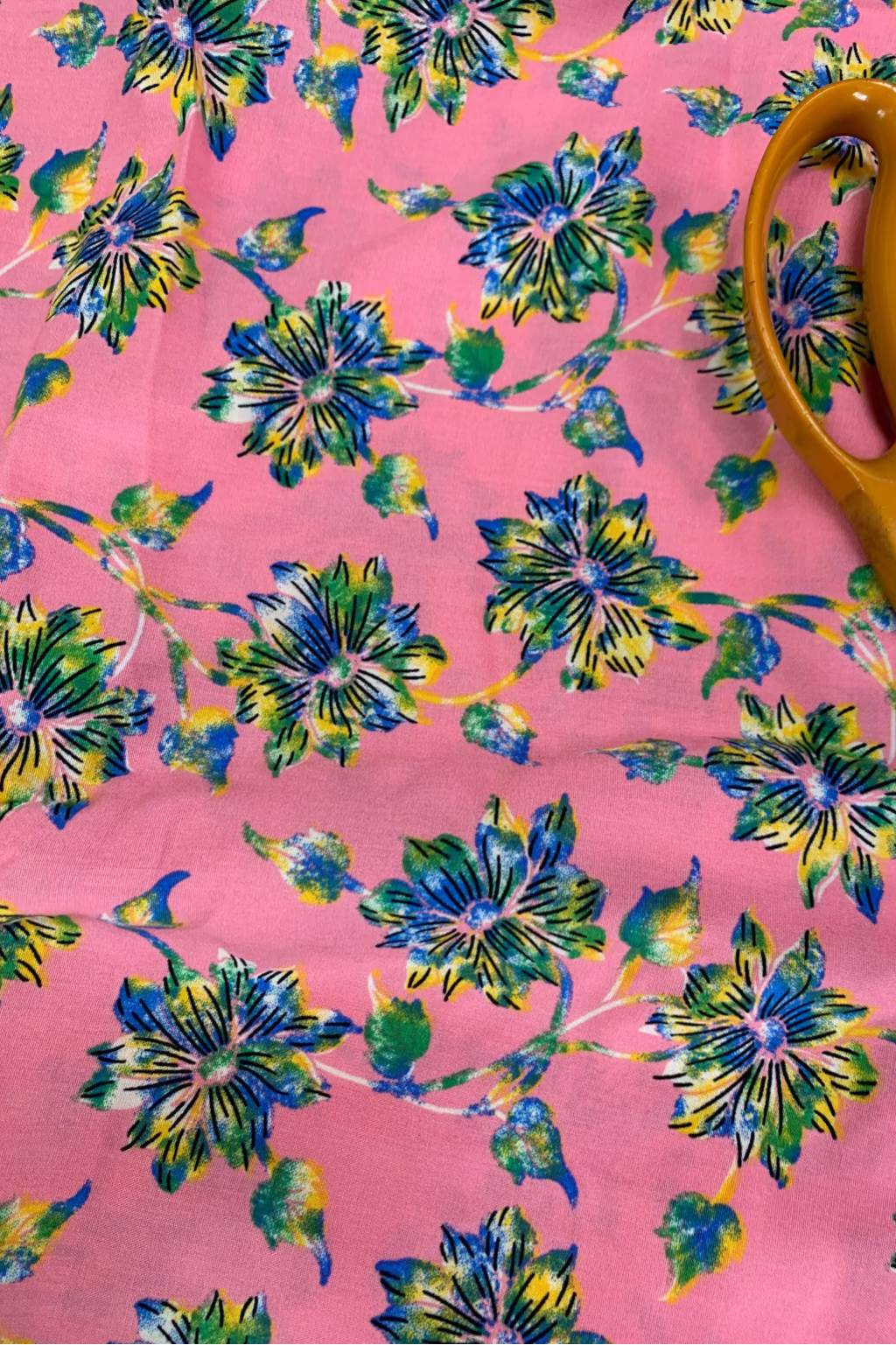 Floral-patterned fabric with blue and green flowers on a pink background, with scissors partially visible.