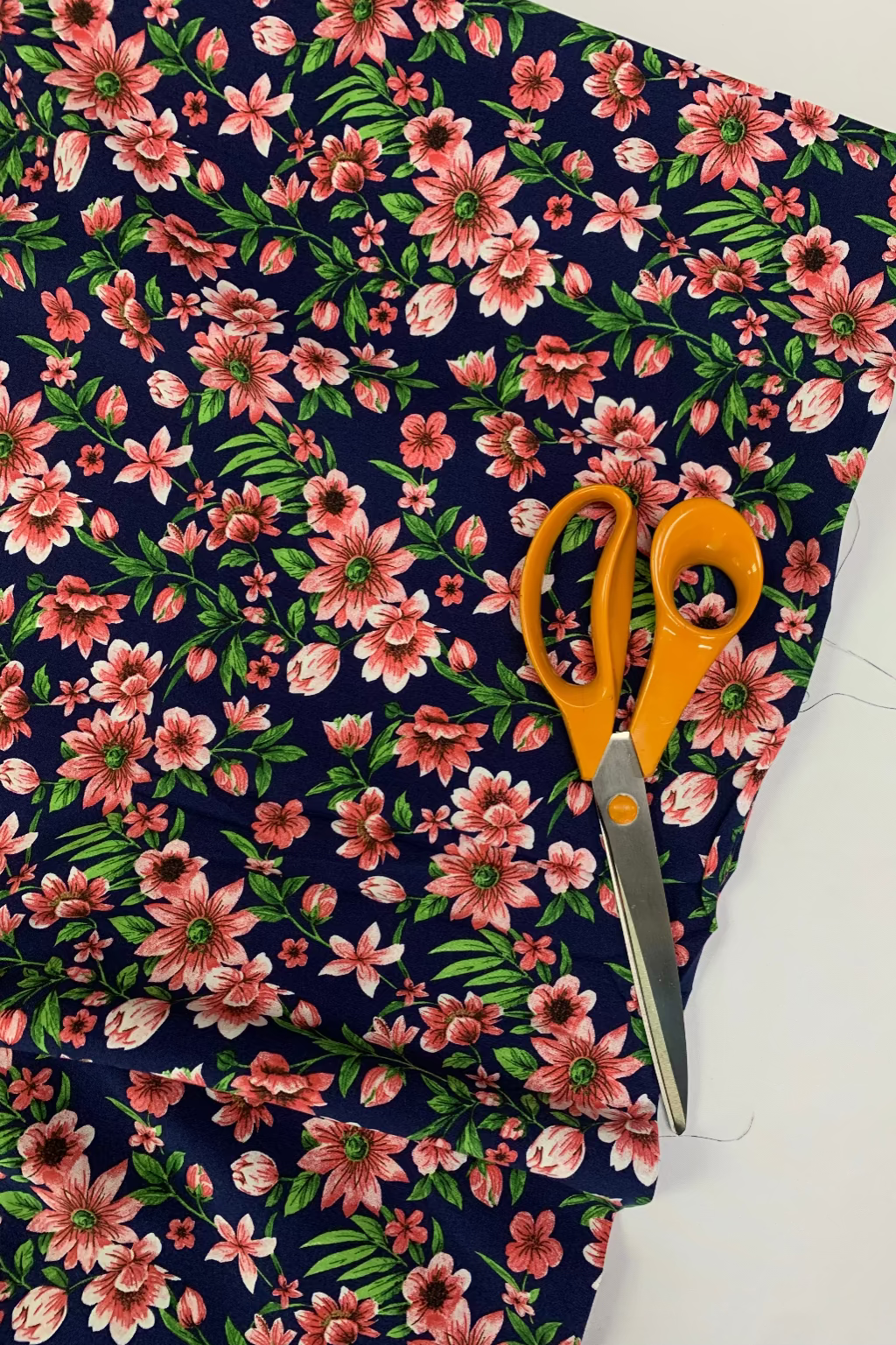 Floral fabric with pink flowers on a dark blue background, cut with orange-handled scissors.