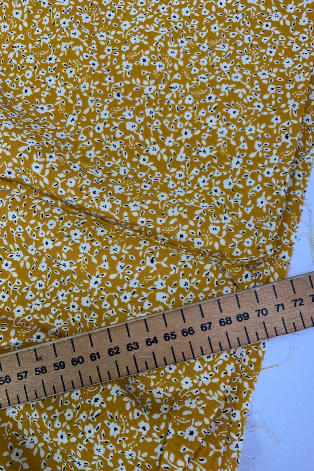 Yellow floral fabric with a ruler for scale on a white background