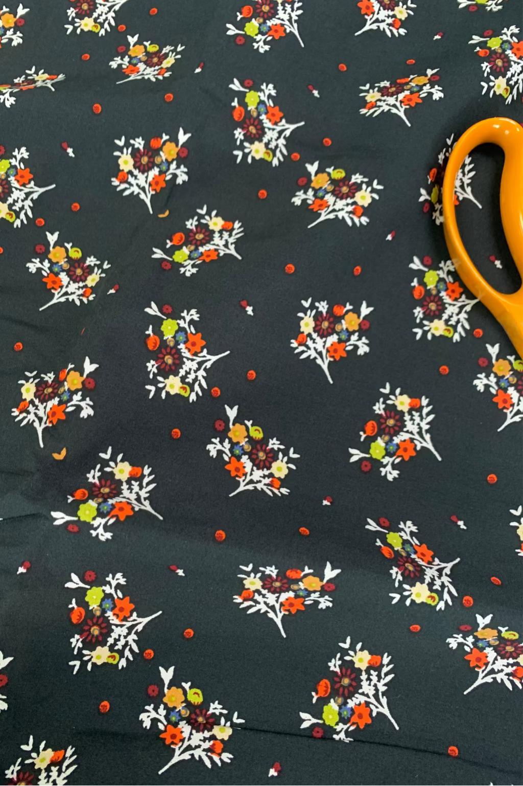 Floral patterned fabric with colorful flowers on a dark background, accompanied by yellow scissors.