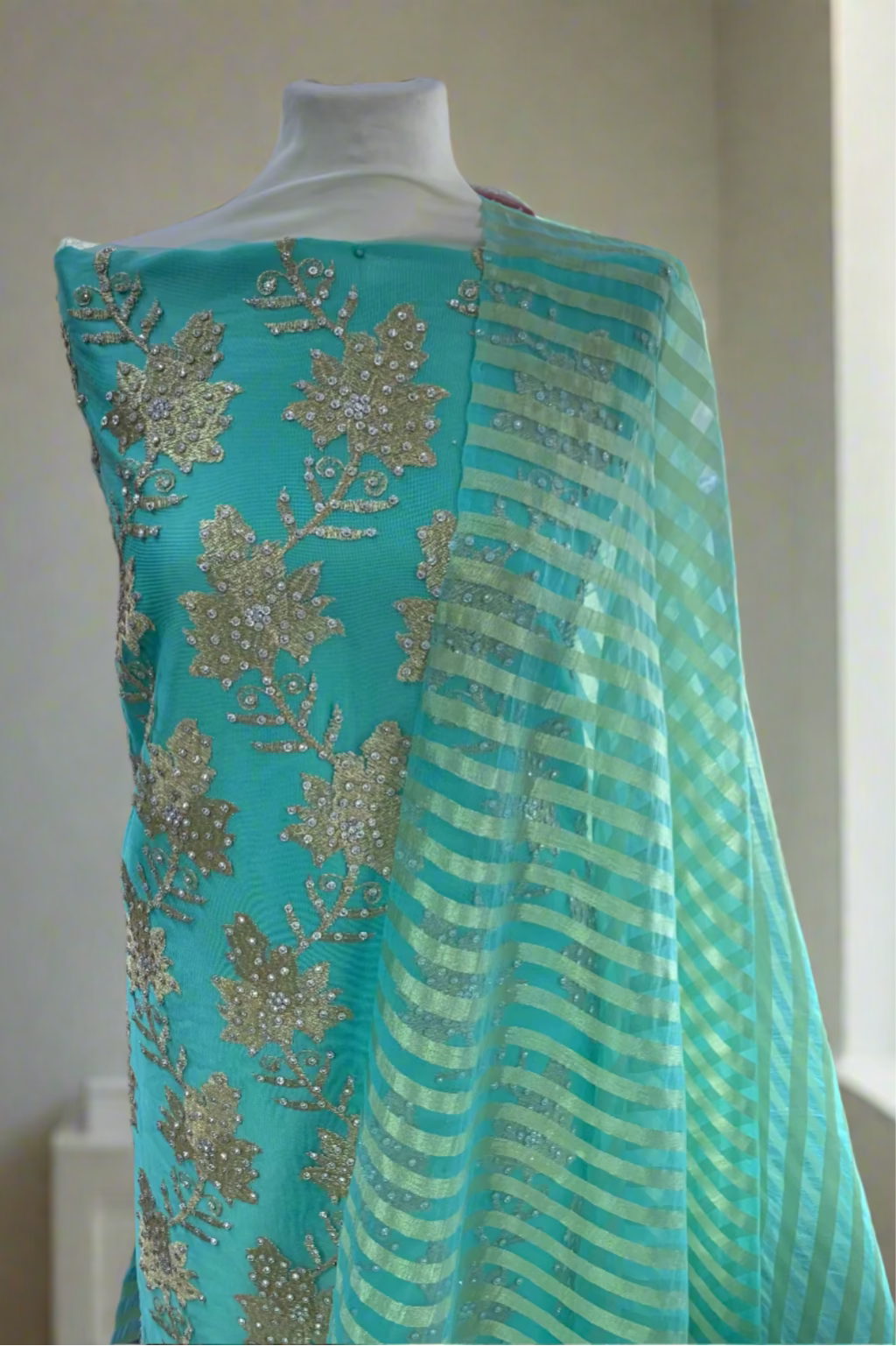 Turquoise fabric with gold embroidery on a mannequin in a store setting.