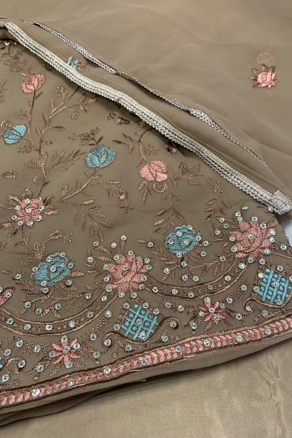 Close-up of a brown fabric with floral embroidery and sequins on a white background