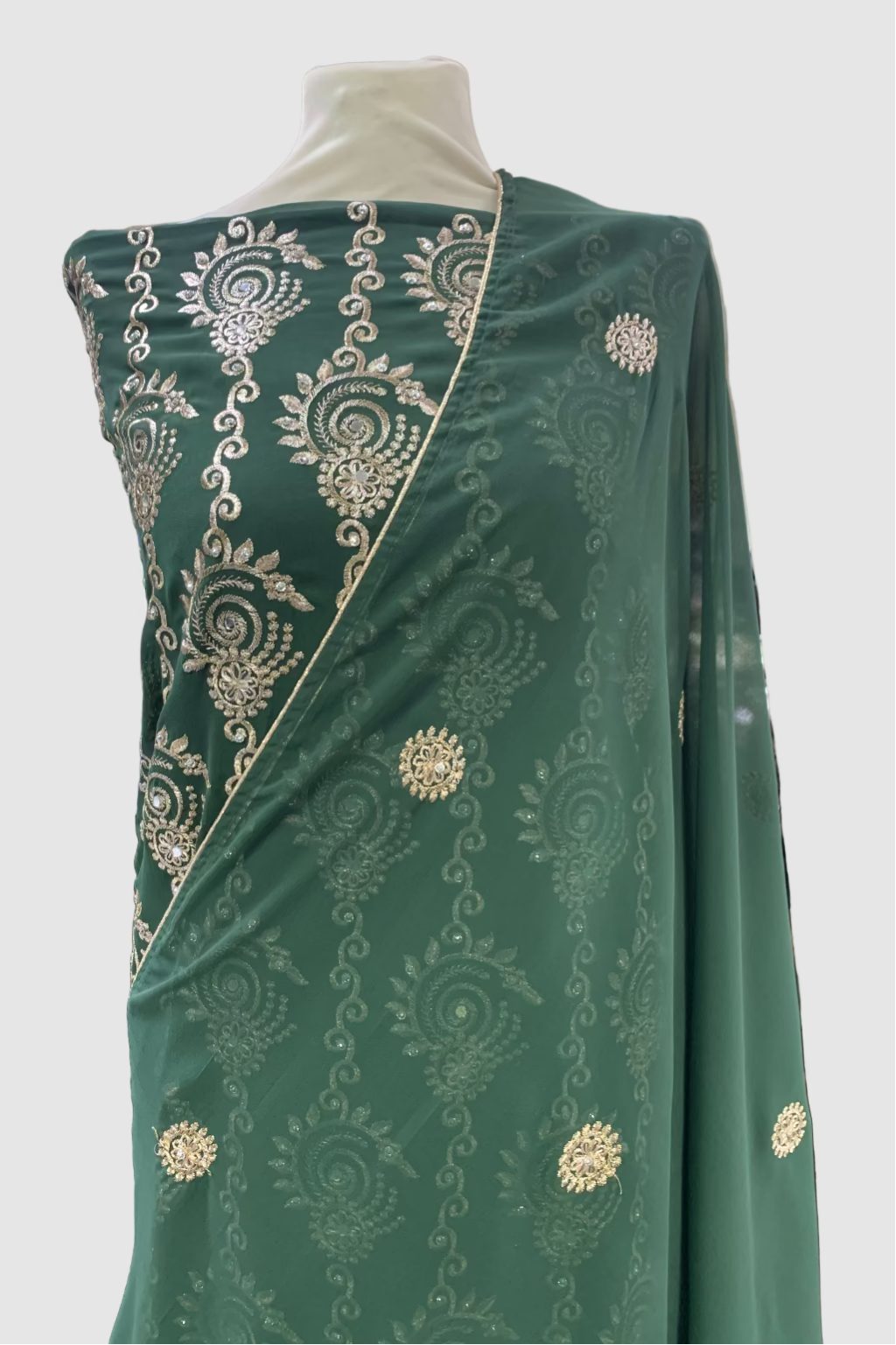 Green fabric with gold embroidery on a mannequin in a store setting