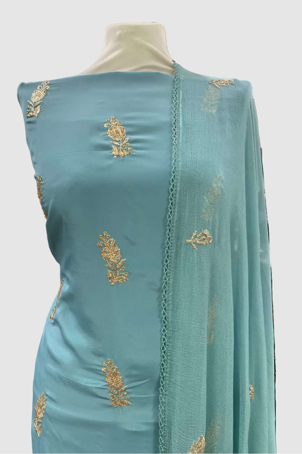 Light blue fabric with gold embroidery on a mannequin in a store setting.