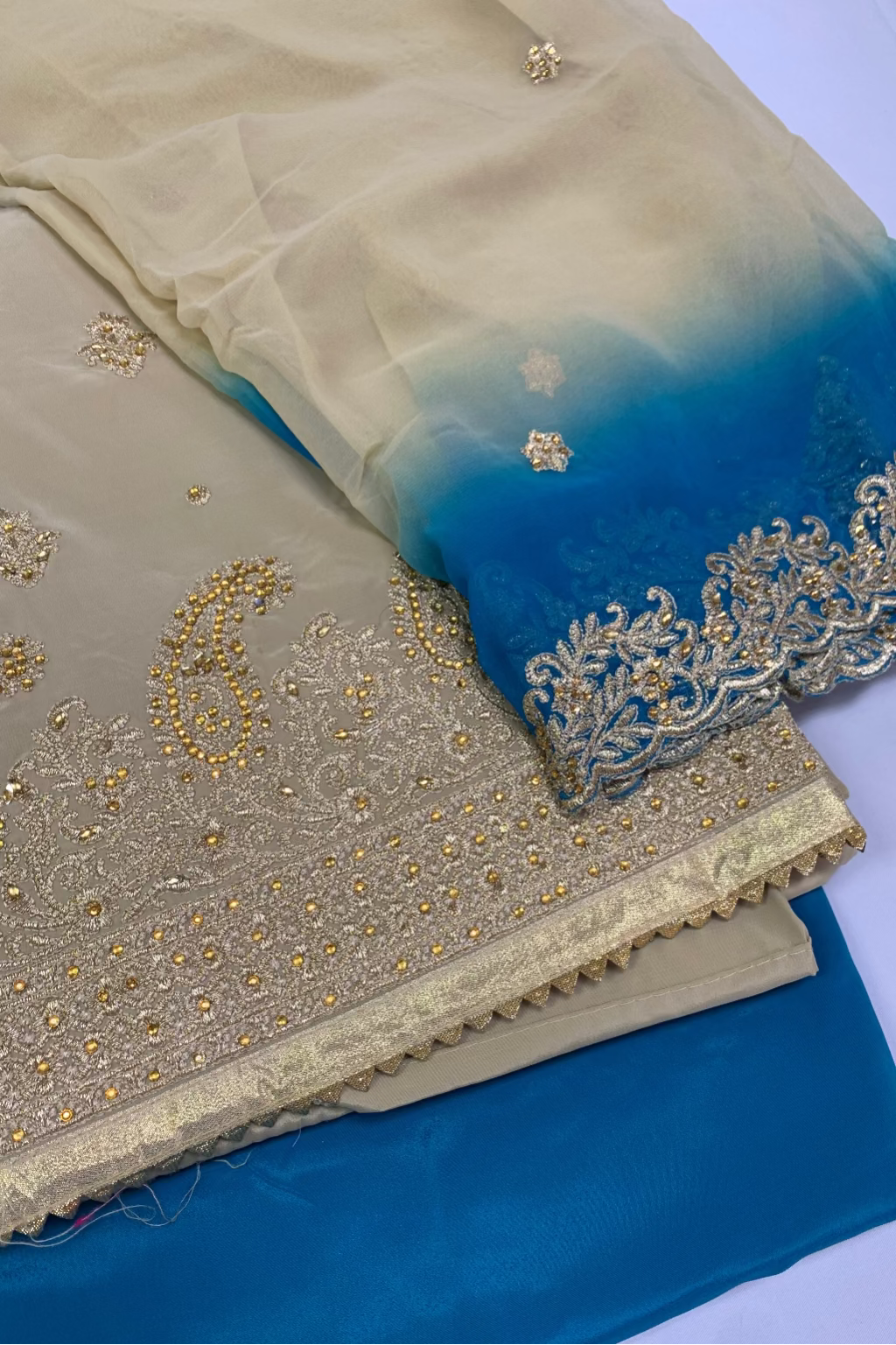Stack of fabric with gold embroidery on a blue and beige background