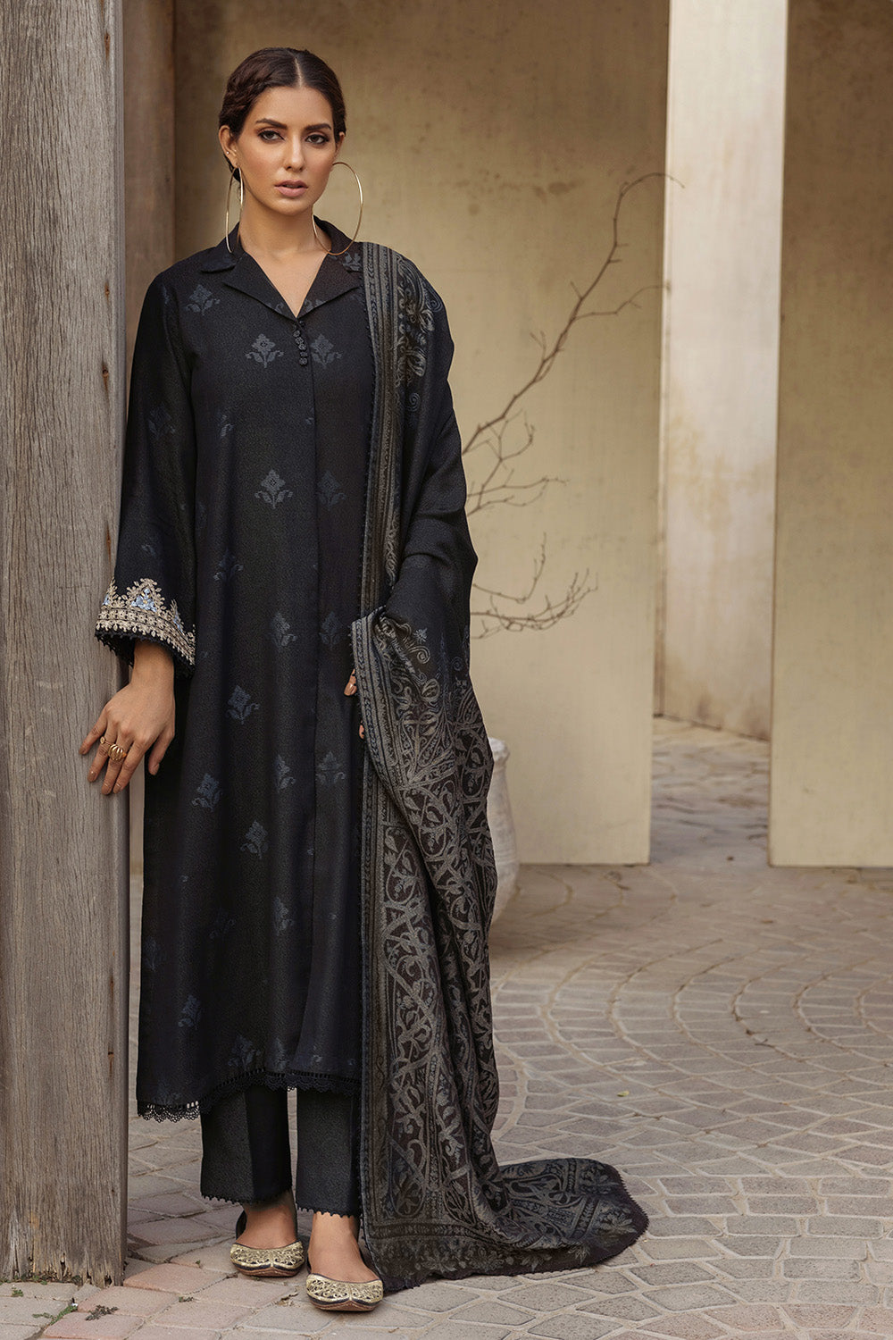A woman wearing a black traditional Karandi Jacquard salwar kameez suit with floral embroidery. She is also holding a dupatta, or scarf, in her left hand.