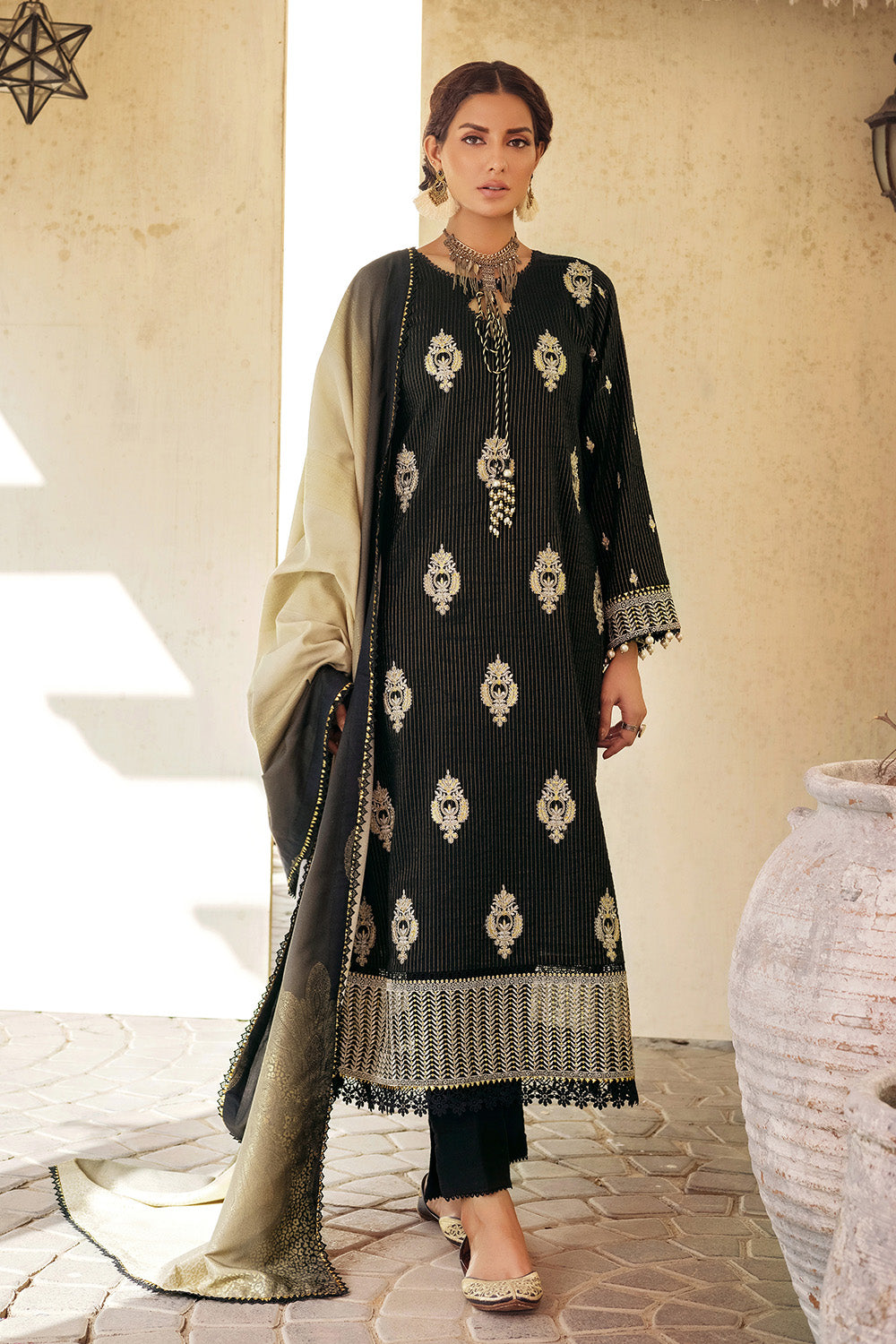 A woman wearing a black and beige traditional salwar kameez suit with embroidered details and a dupatta.