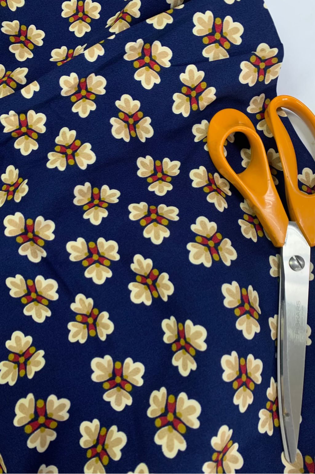 Floral-patterned fabric with a pair of orange-handled scissors on top