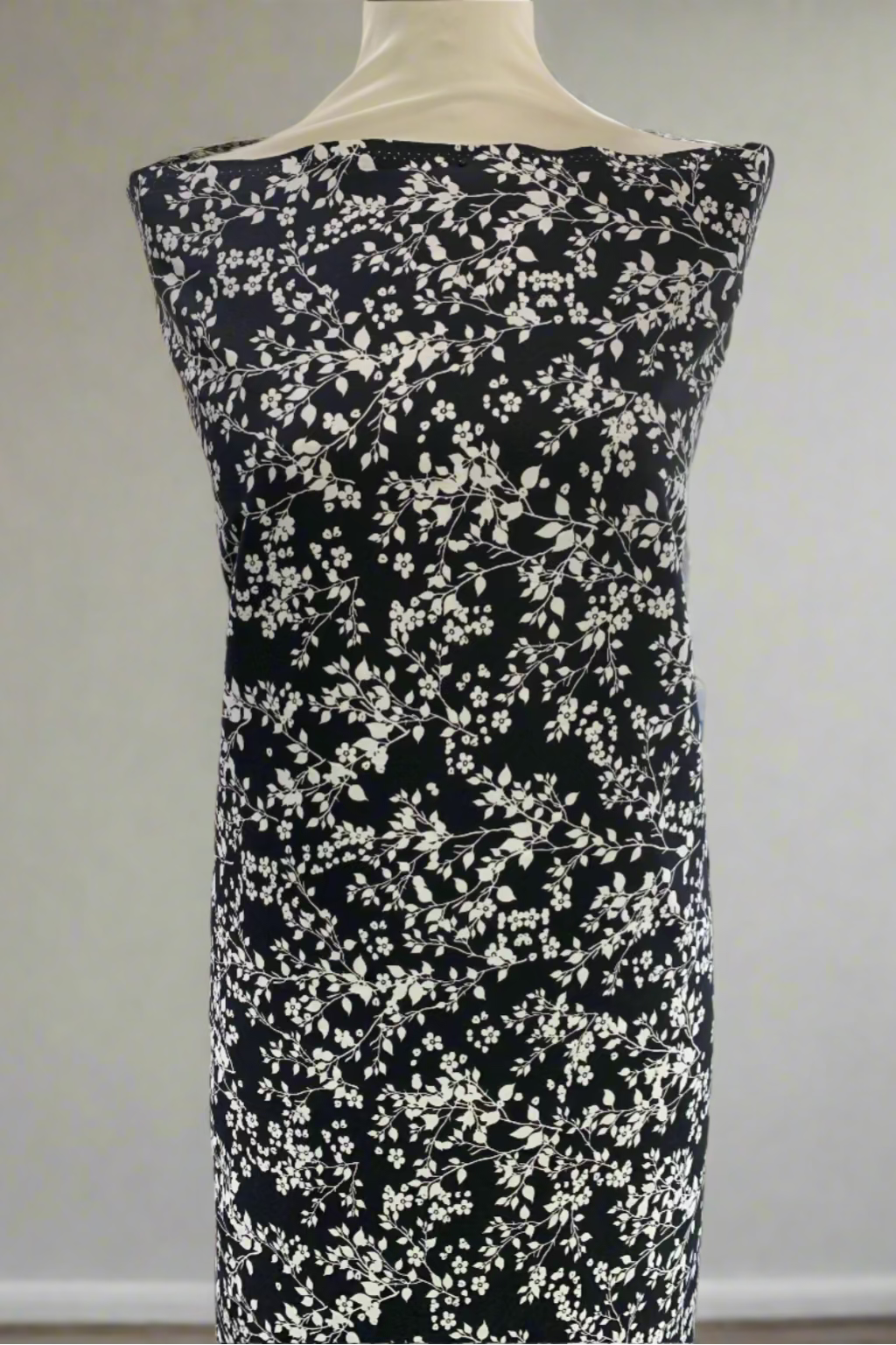 Black dress fabric with white floral pattern on a mannequin in a store setting.