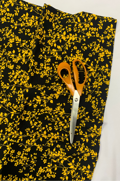 Black fabric with yellow floral pattern and a pair of scissors on a white background