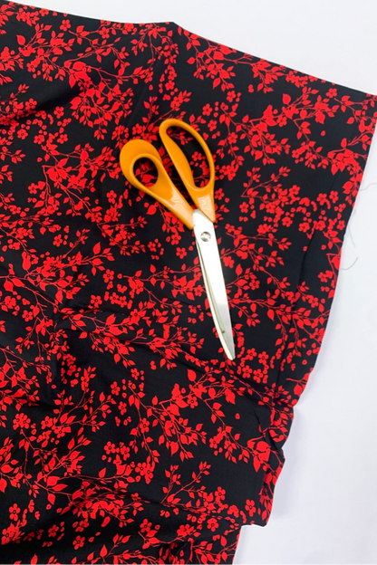 Pair of orange-handled scissors on a black fabric with red floral pattern