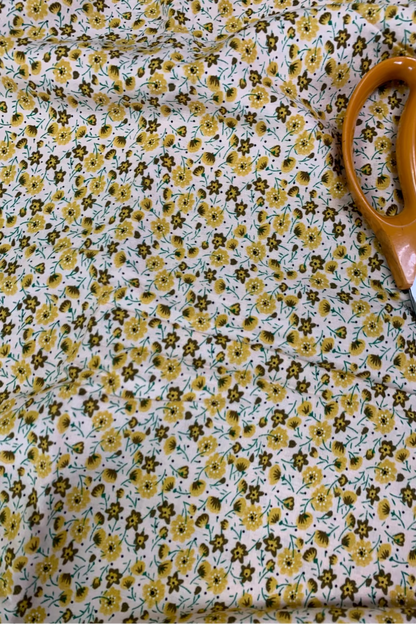 Floral fabric with yellow flowers and green leaves, accompanied by a pair of scissors.