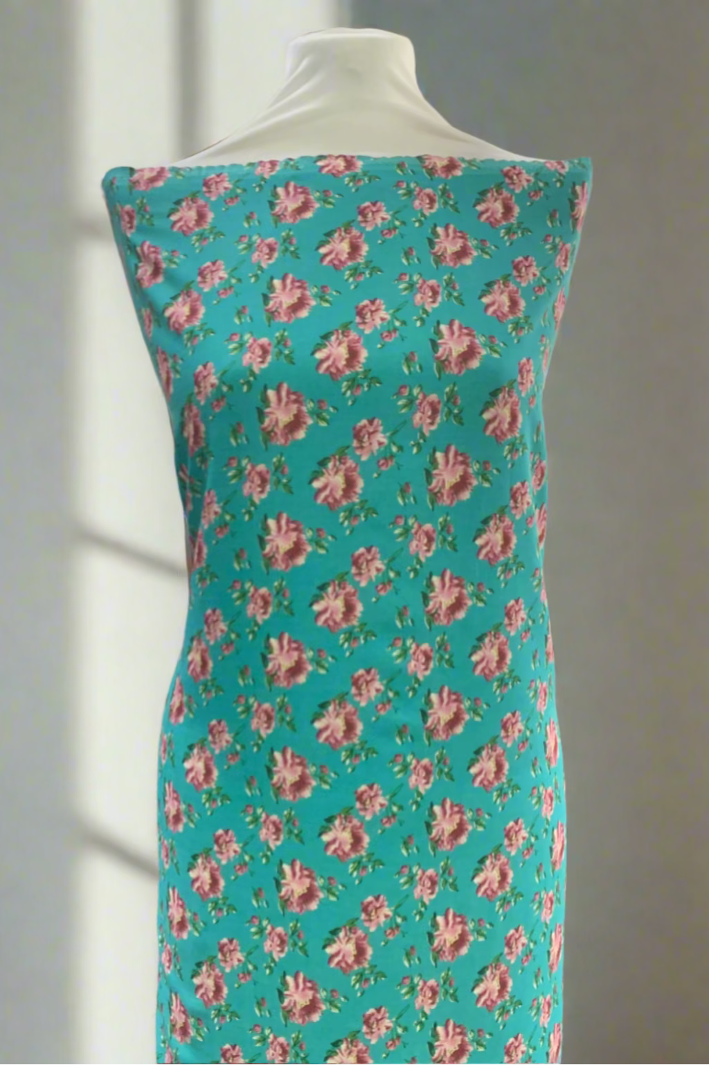 Mannequin wearing a floral dress with pink roses on a turquoise background in a store setting.