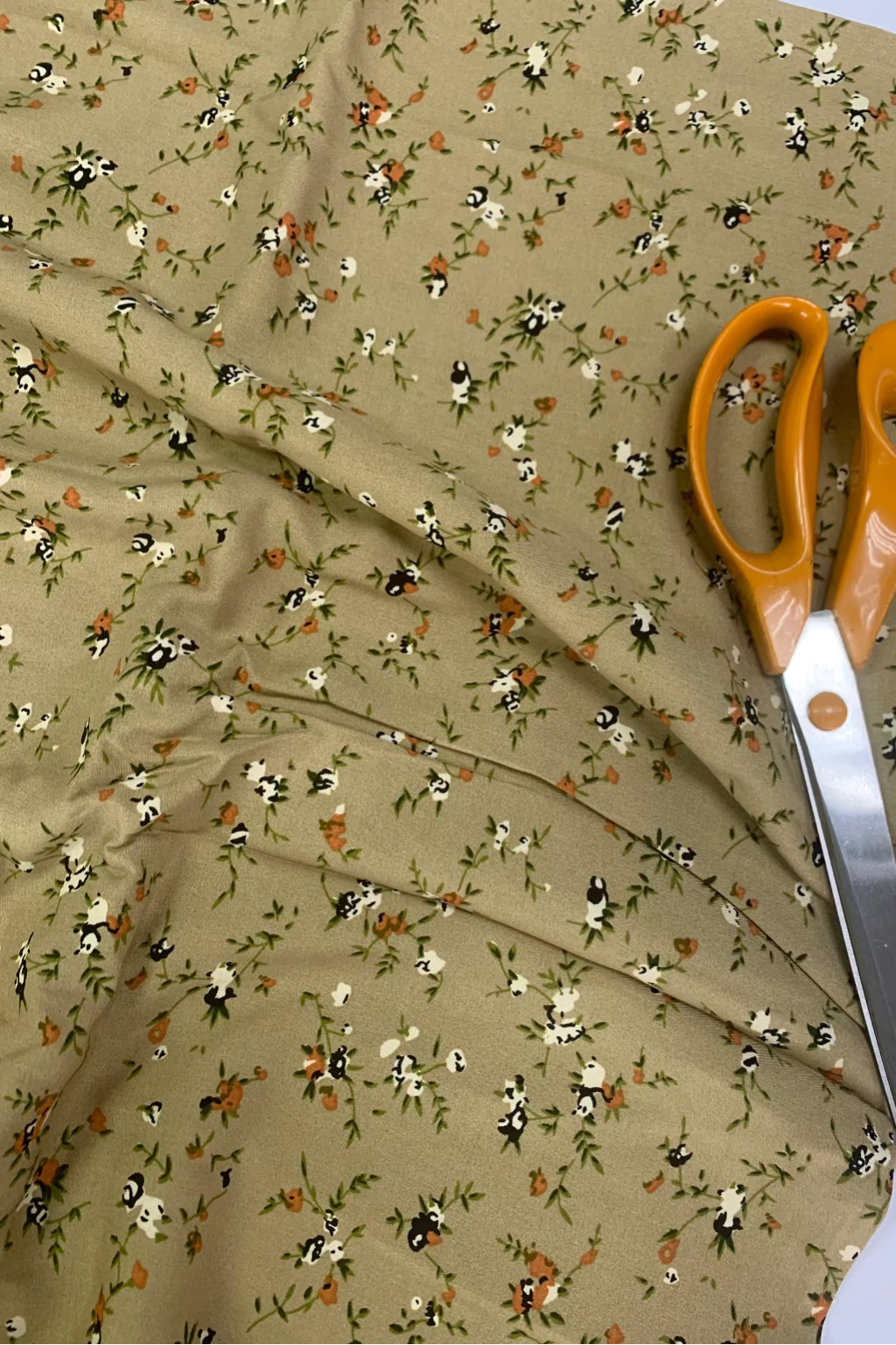 Floral fabric with a pair of orange-handled scissors on top