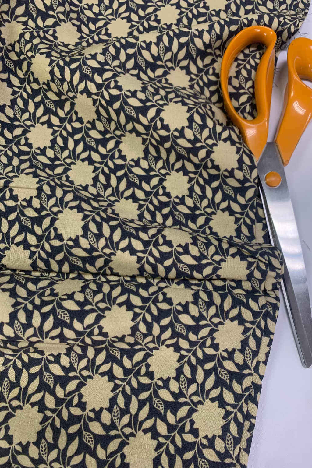 Floral-patterned fabric with orange-handled scissors on a white background