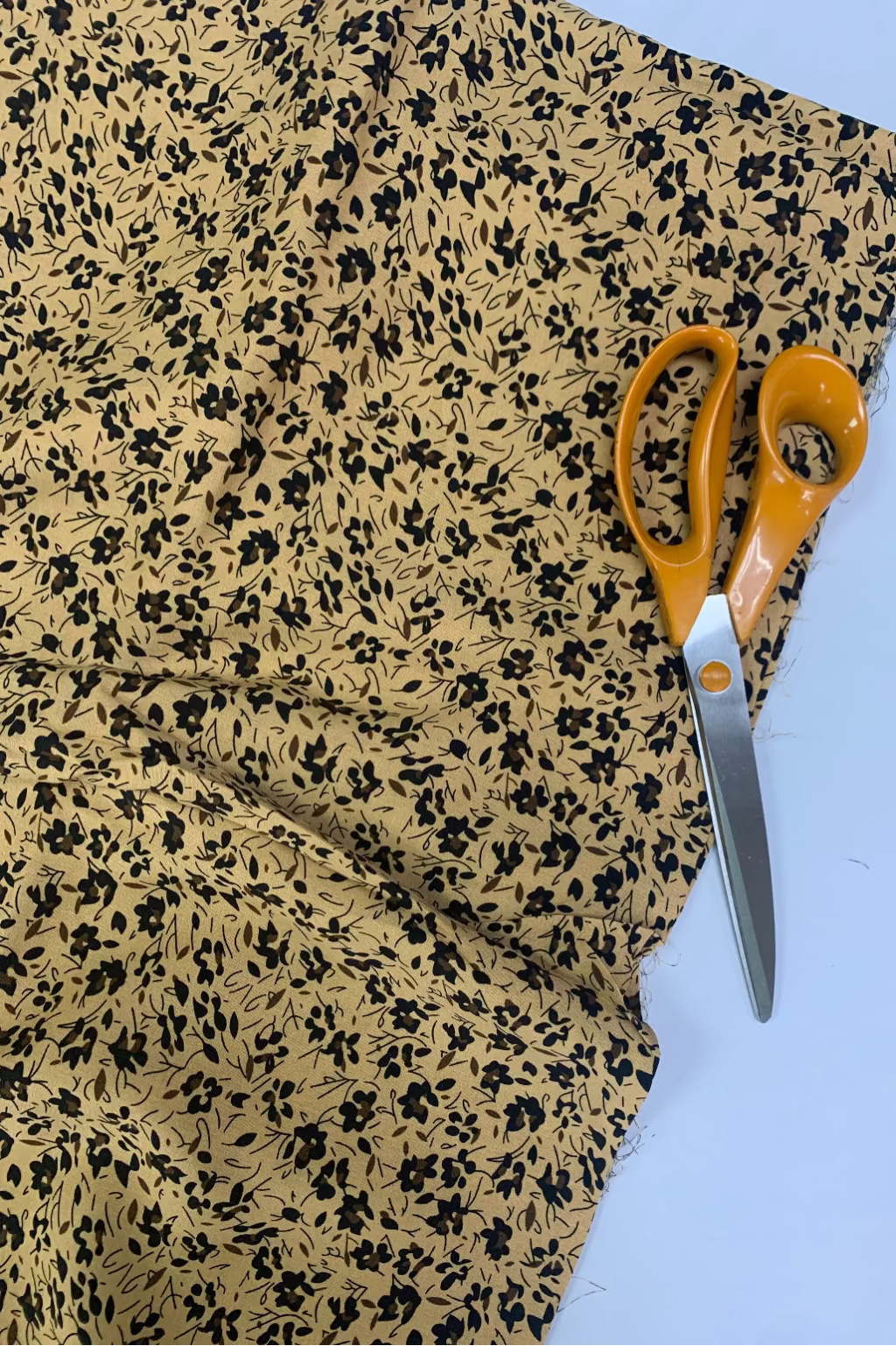 Fabric with black floral pattern and orange-handled scissors on a light blue background
