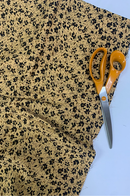 Fabric with black floral pattern and orange-handled scissors on a light blue background