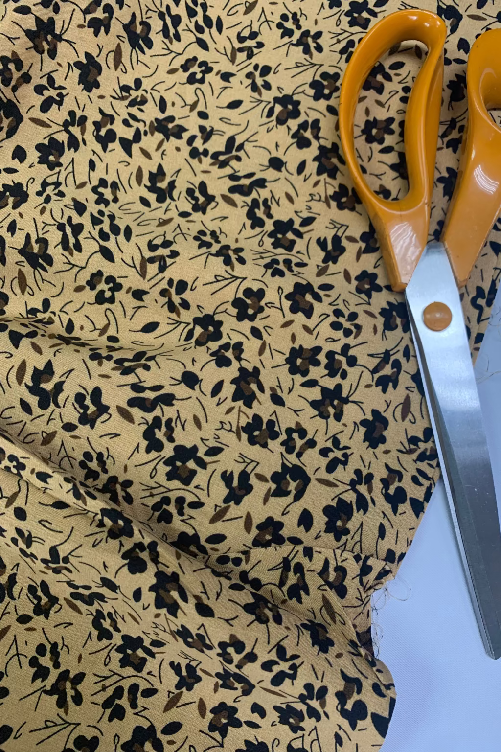 Scissors with orange handles on a floral fabric background