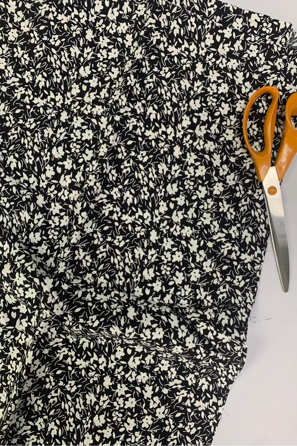 Black and white floral fabric with a pair of orange-handled scissors on a white background
