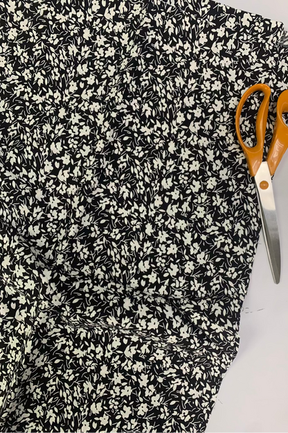 Black and white floral fabric with a pair of orange-handled scissors on a white background