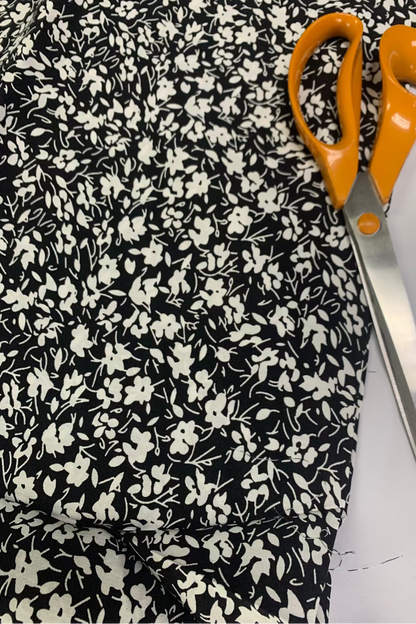 Scissors with orange handles on a black floral fabric