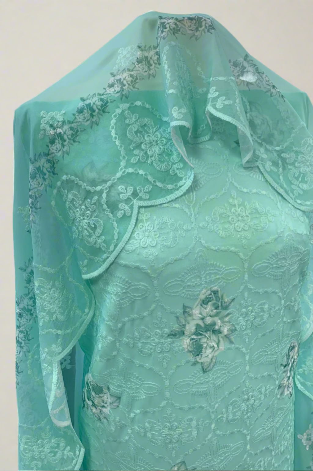 Turquoise fabric with floral embroidery draped over a mannequin in an indoor setting.
