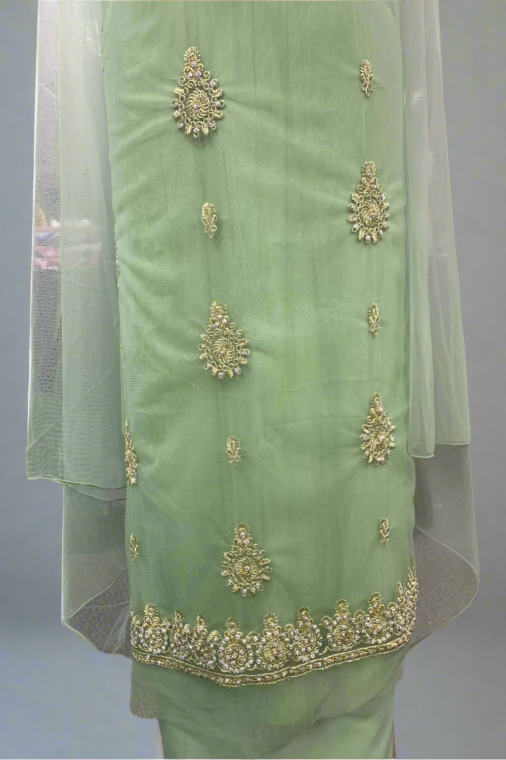Light green traditional outfit with gold embroidery in a store setting
